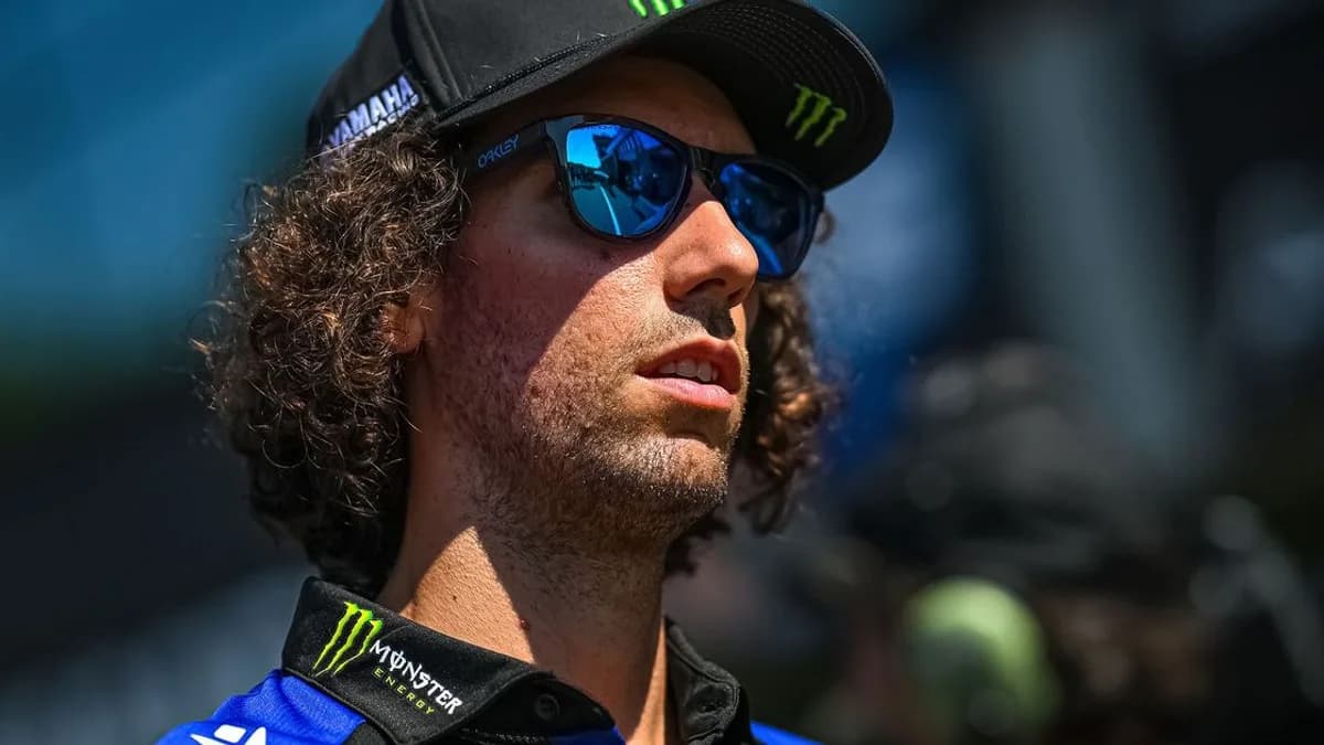 Alex Rins wears a blue Yamaha cap and blue sunglasses in a close-up portrait