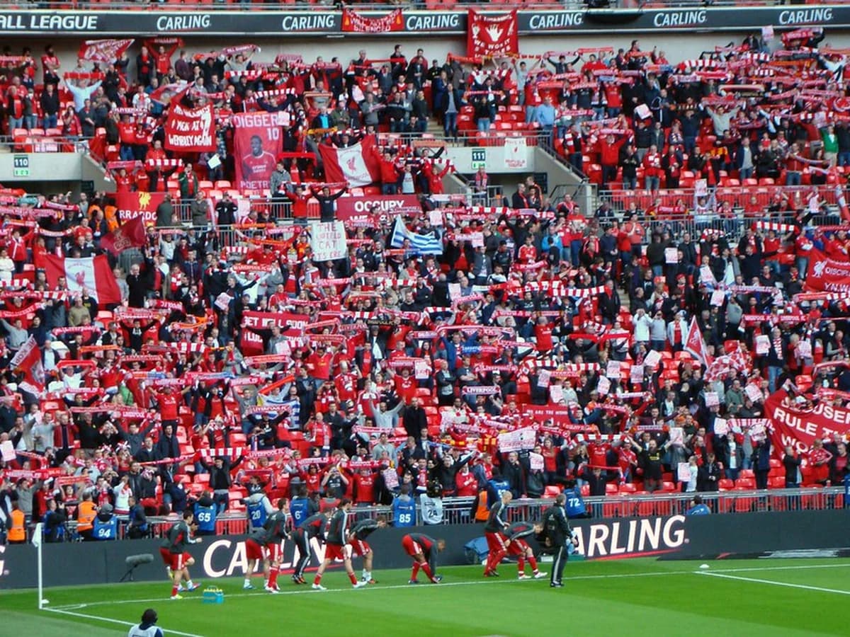 Fans in a packed stadium stand holding up scarves