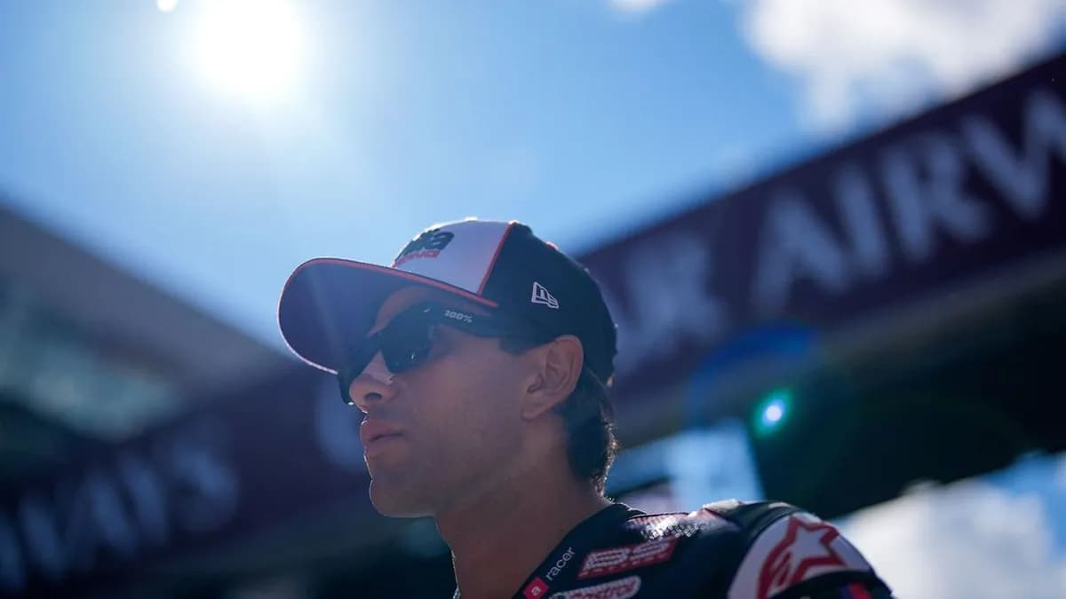 Jorge Martin in an Aprilia cap and dark sunglasses looks ahead under a bright blue sky in the Red Bull Ring paddock