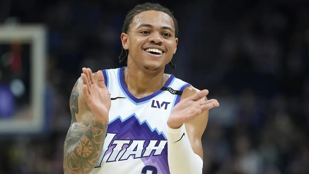 Keyonte George smiles and claps in a white and purple Utah Jazz jersey during a game