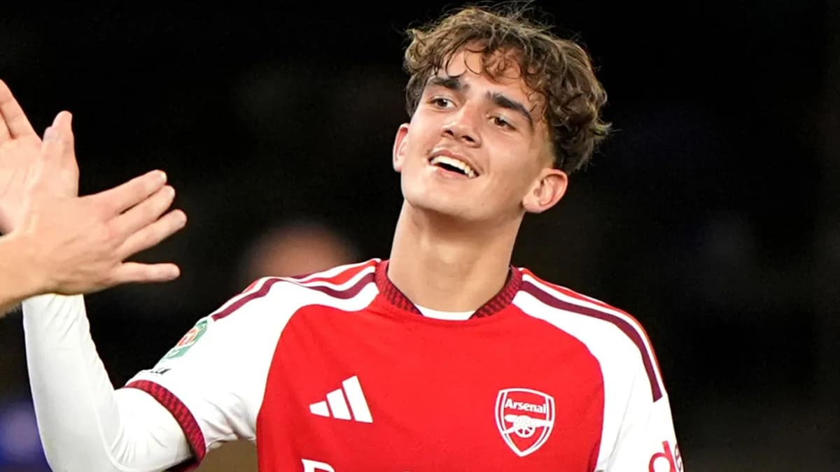 Max Dowman smiles and raises his hand in a red and white Arsenal shirt