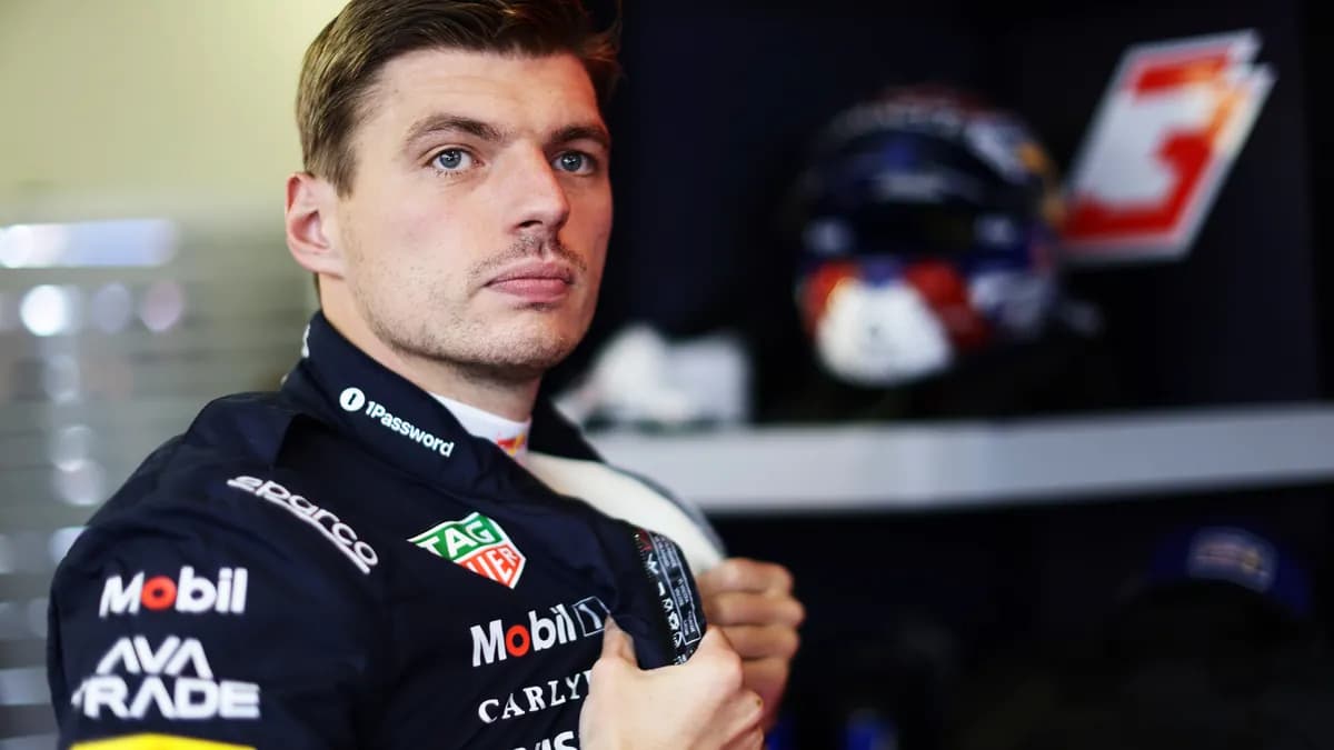 Max Verstappen in his navy Red Bull race suit stands in the team garage in Baku with his helmet on a shelf behind him