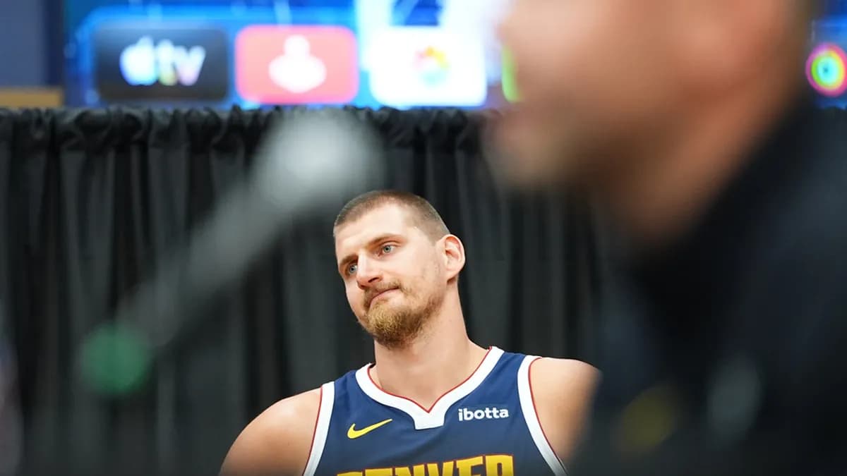 Nikola Jokic in a navy Denver Nuggets jersey listens to a question at the team’s 2026 media day