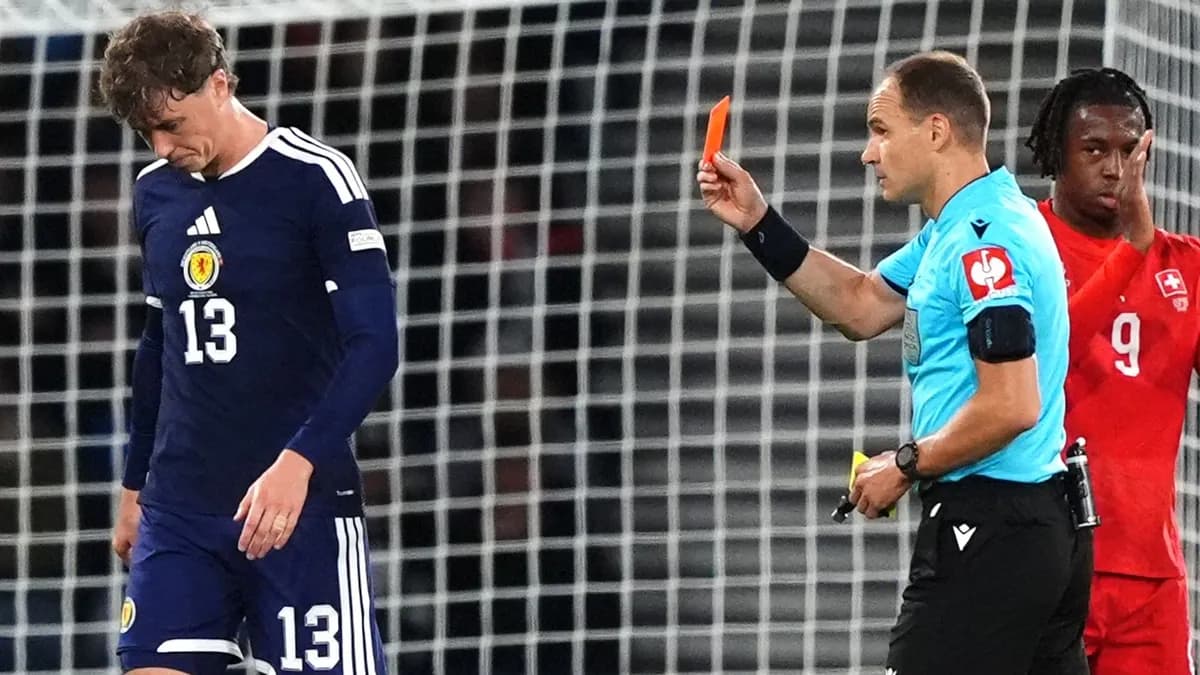 Scotland defender Jack Hendry looks down as the referee shows a red card, with a Switzerland player in red standing nearby at Hampden Park
