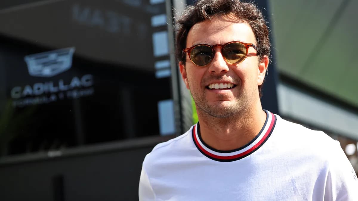 Sergio Perez smiles in sunglasses and a white T-shirt outside the Cadillac Formula 1 team building in the Baku paddock