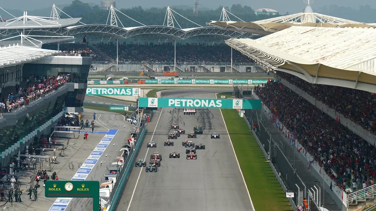 Formula 1 cars head down the Sepang start-finish straight beneath the Petronas gantry and packed grandstands at a Malaysian Grand Prix start